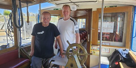 Zwei Männer, die Crewmitglieder des Schiffs „Wilde Ilse“, stehen vor dem Steuerrad.