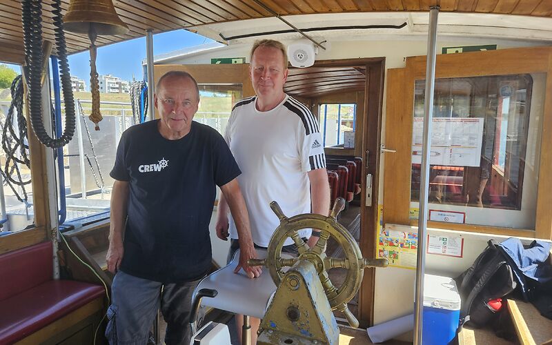 Zwei Männer, die Crewmitglieder des Schiffs „Wilde Ilse“, stehen vor dem Steuerrad.