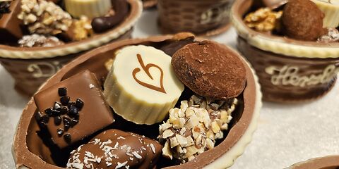 Bunte Pralinen aus weißer, Milch- und dunkler Schokolade liegen als Geschenk in dekorativen Schokokörben.