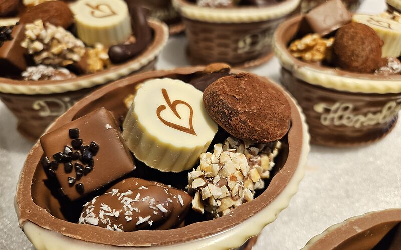 Bunte Pralinen aus weißer, Milch- und dunkler Schokolade liegen als Geschenk in dekorativen Schokokörben.