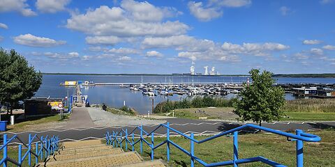 Blick auf den Hafen am Bärwalder See mit zahlreichen Booten. Im Vordergrund führt eine breite Treppe mit blauem Geländer vom Parkplatz hinunter zum Hafen.