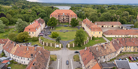 Luftaufnahme einer historischen Schlossanlage. Im Mittelpunkt sind die Ruinen des ehemaligen Schlosses des Grafen Brühl zu sehen. Daneben stehen historische Wirtschaftsgebäude, die heute für einen Hotelbetrieb und für kulturelle Veranstaltungen genutzt werden. Die Gebäude liegen in einer weitläufigen, begrünten Anlage.
