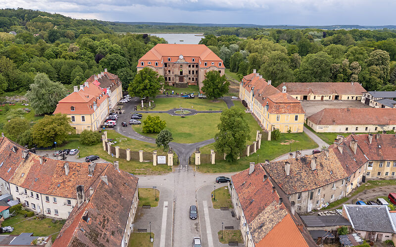 Luftaufnahme einer historischen Schlossanlage. Im Mittelpunkt sind die Ruinen des ehemaligen Schlosses des Grafen Brühl zu sehen. Daneben stehen historische Wirtschaftsgebäude, die heute für einen Hotelbetrieb und für kulturelle Veranstaltungen genutzt werden. Die Gebäude liegen in einer weitläufigen, begrünten Anlage.