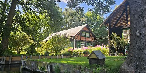 Typisches Spreewaldhaus am Wasser, umgeben von grüner Landschaft, gesehen von einem Kahn.