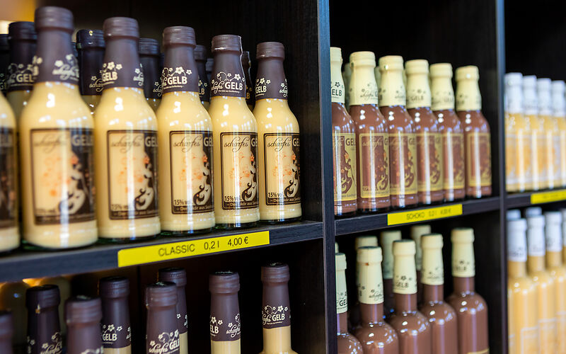 Mehrere bunte Flaschen Eierlikör der Firma scharfesGELB nebeneinander aufgereiht. Die Etiketten sind farbig und unterschiedlich gestaltet.