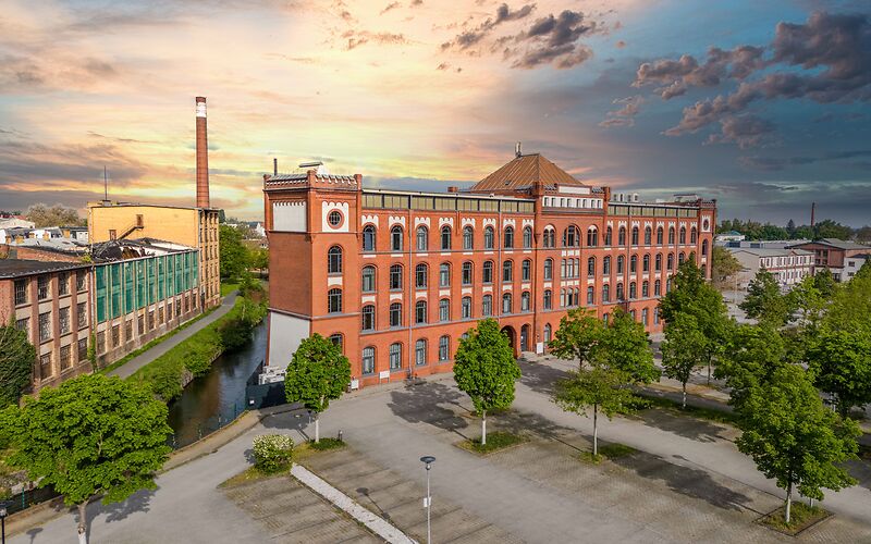 Der Sitz des Landkreises Spree-Neiße in der ehemaligen Tuchfabrik Robert Cattien aus roten Ziegeln, daneben das Heizkraftwerk Avellis mit hohem Schornstein bei Sonnenuntergang.