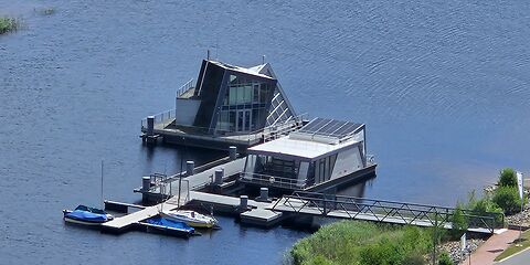 Auf dem Foto sind zwei moderne Gebäude auf dem Bergheider See aus der Vogelperspektive zu sehen: ein Aquaforum und ein schwimmendes Haus.
