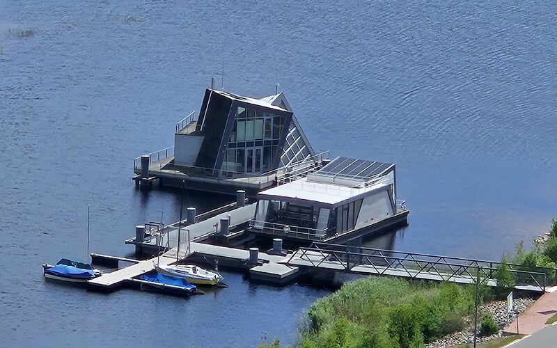 Auf dem Foto sind zwei moderne Gebäude auf dem Bergheider See aus der Vogelperspektive zu sehen: ein Aquaforum und ein schwimmendes Haus.