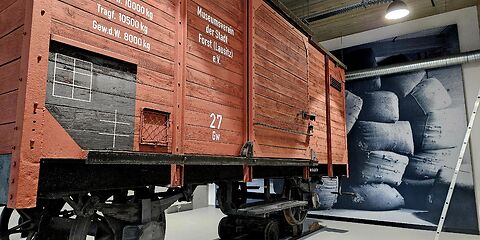 Im Vordergrund steht ein rotbrauner Kohlenwagen, der auf Rollböcken eingesetzt ist. Auf dem Wagen sind die Aufschriften „Ladegewicht 10.000 kg“, „Tragfähigkeit 10.500 kg“ sowie „Museumsverein der Stadt Forst (Lausitz)“ zu lesen. Im Hintergrund ist eine große schwarz-weiße Fotowand mit voll gefüllten Säcken zu sehen.