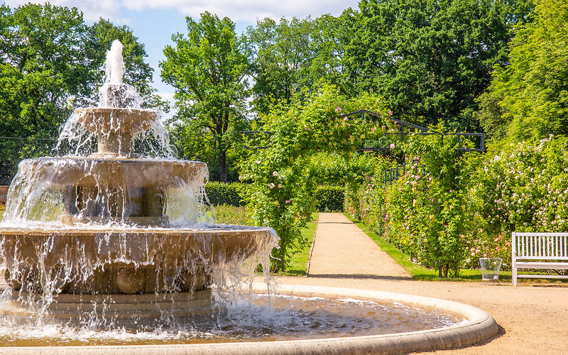 Im Vordergrund Kaskadenbrunnen und rechts im Hintergrund ein Rosenbogen