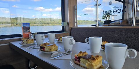 Ein gedeckter Tisch mit Kaffee und Kuchen, vorbereitet für die Reisegruppe. Für jede Person sind drei verschiedene Kuchensorten vorgesehen.