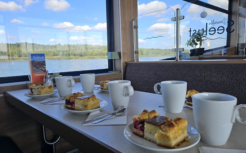 Ein gedeckter Tisch mit Kaffee und Kuchen, vorbereitet für die Reisegruppe. Für jede Person sind drei verschiedene Kuchensorten vorgesehen.