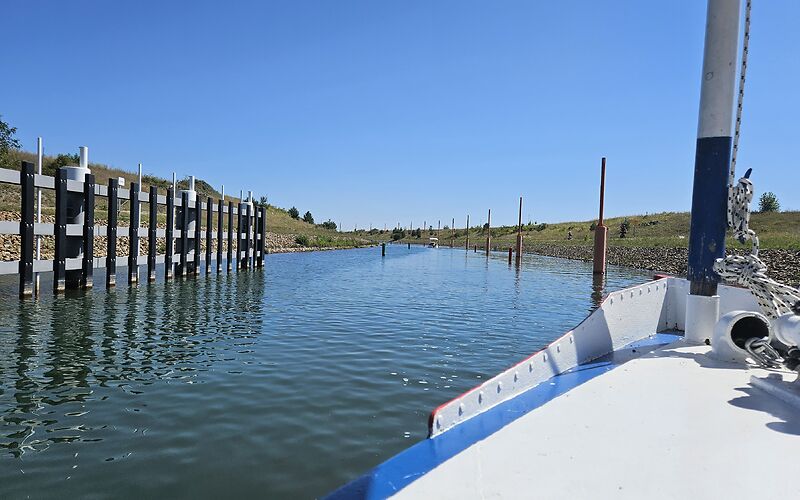 Eine Schifffahrt durch den Ilse-Kanal. Das Schiff fährt aus einem Tunnel auf das Wasser hinaus. Links und rechts des Kanals stehen grüne und rote Pfähle.