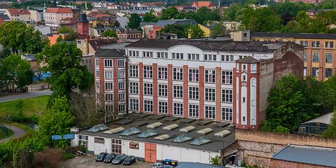 Auf dem Foto ist eine große Fabrik zu sehen, der frühere Sitz der Firma Hänsel & Co. Das Gebäude ist dreietagig. Die Fassade besteht aus weißen und dunkelroten Brandziegeln.