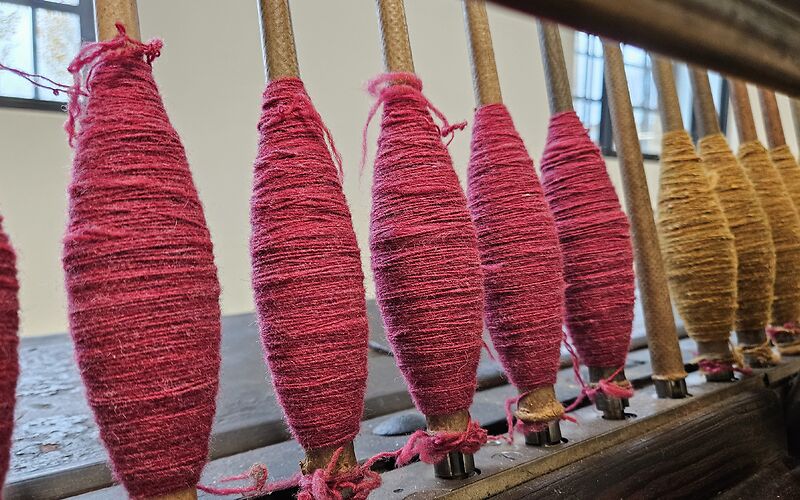 Auf dem Foto sind rote und gelbe historische Wollfäden auf Spulen aufgerollt zu sehen.