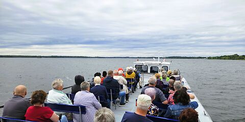 Touristen genießen die Fahrt auf dem Senftenberger See vom Oberdeck des Fahrgastschiffes aus. Sie sitzen an Deck und schauen über das Wasser und die umliegende Landschaft. Dabei genießen sie die Aussicht und die entspannte Atmosphäre während der Schifffahrt.