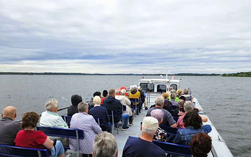 Touristen genießen die Fahrt auf dem Senftenberger See vom Oberdeck des Fahrgastschiffes aus. Sie sitzen an Deck und schauen über das Wasser und die umliegende Landschaft. Dabei genießen sie die Aussicht und die entspannte Atmosphäre während der Schifffahrt.