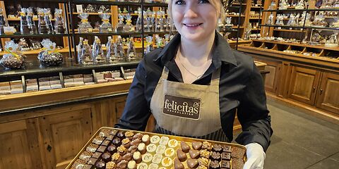 Im SchokoLaden der Confiserie Felicitas in Hornow präsentiert eine Frau auf einem Tablet eine Auswahl verschiedener Pralinen. Im Hintergrund sind mehrere Figuren aus Schokolade zu sehen.