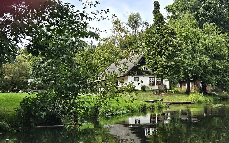 Blick vom Spreekanal auf ein traditionelles Spreewaldhaus, das von einem schönen, grünen Grundstück umgeben ist.