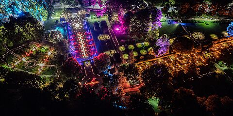 Das Bild zeigt den Rosengarten in Forst (Lausitz) während der Rosengartenfesttage bei Nacht aus der Vogelperspektive. Thematisch gestaltete Gartenbereiche sind durch bunte Lichtinstallationen stimmungsvoll hervorgehoben.
