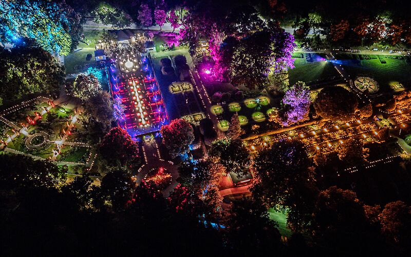 Das Bild zeigt den Rosengarten in Forst (Lausitz) während der Rosengartenfesttage bei Nacht aus der Vogelperspektive. Thematisch gestaltete Gartenbereiche sind durch bunte Lichtinstallationen stimmungsvoll hervorgehoben.