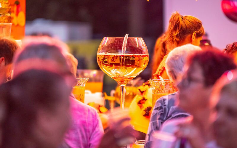 ein Stimmungsbild mit einem großen Coktailglas in der Mitte, drumherum Menschen, die sich unterhalten
