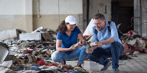 Zwei Personen, eine Frau und ein Mann, knien und betrachten Textilstoffabfälle.