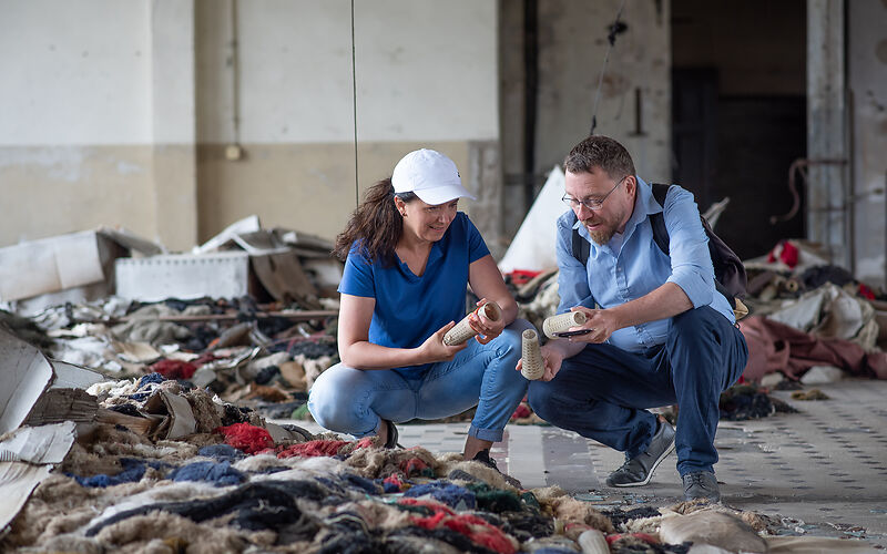 Zwei Personen, eine Frau und ein Mann, knien und betrachten Textilstoffabfälle.