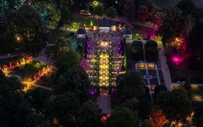 Luftbild auf den mit bunten Lichtern erleuchteten Rosengarten bei Dunkelheit.