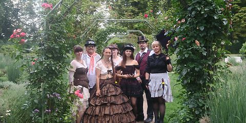 historisch gekleidete Gruppe aus dem Viktorianischen Zeitalterstehen unter einen blühenden Rosenbogen