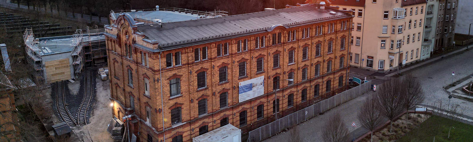Fotograf: Frank Junge, Bildrechte: Frank Junge Vor dem Textilmuseum, einem alten Steingebäude, ist vor dem Gehweg ein Bauzaun aufgestellt worden. Das kleinere Nebengebäude hinter dem Museum ist mit einem Gerüst umstellt. Über den Hof des Museums verlaufen zwei Schienen, die in der Mitte des Hofes ineinander übergehen